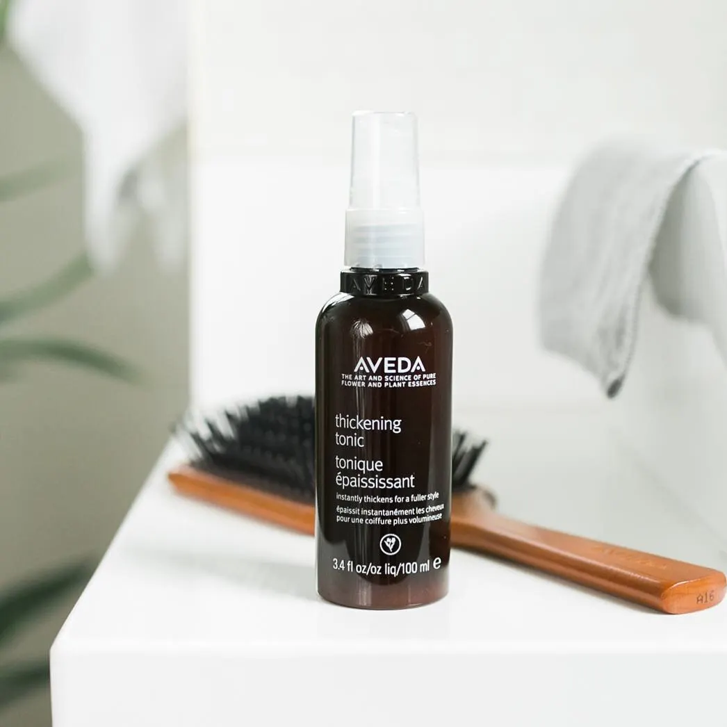 Flacon Aveda Thickening Tonic posé devant une brosse à cheveux en bois