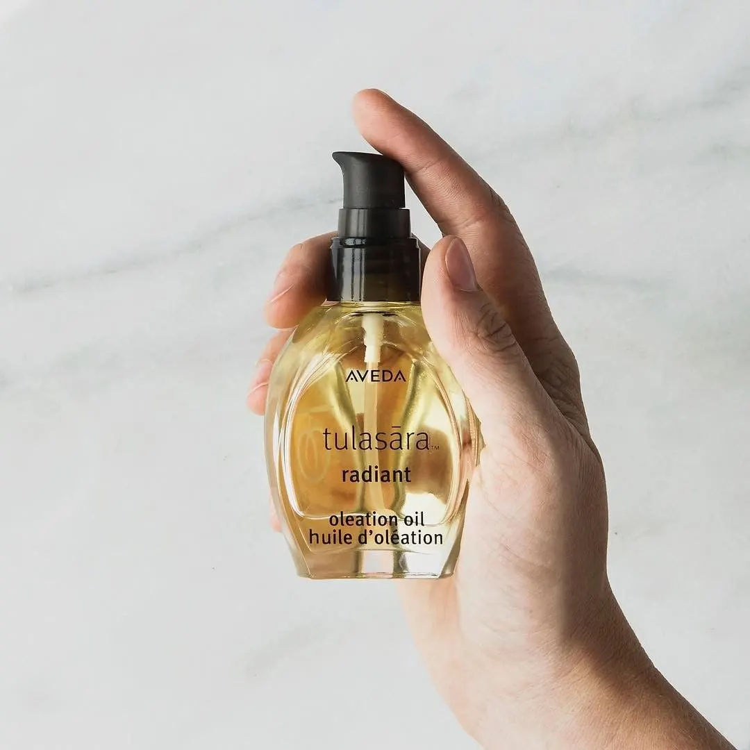 Flacon d’huile d’oléation Tulasara Radiant d’Aveda tenu dans une main