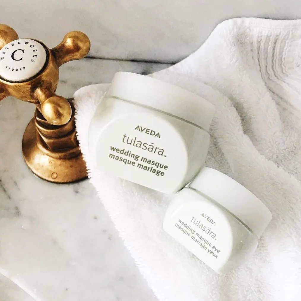 Masques visage Aveda Tulasara disposés sur des serviettes blanches avec un outil de massage doré