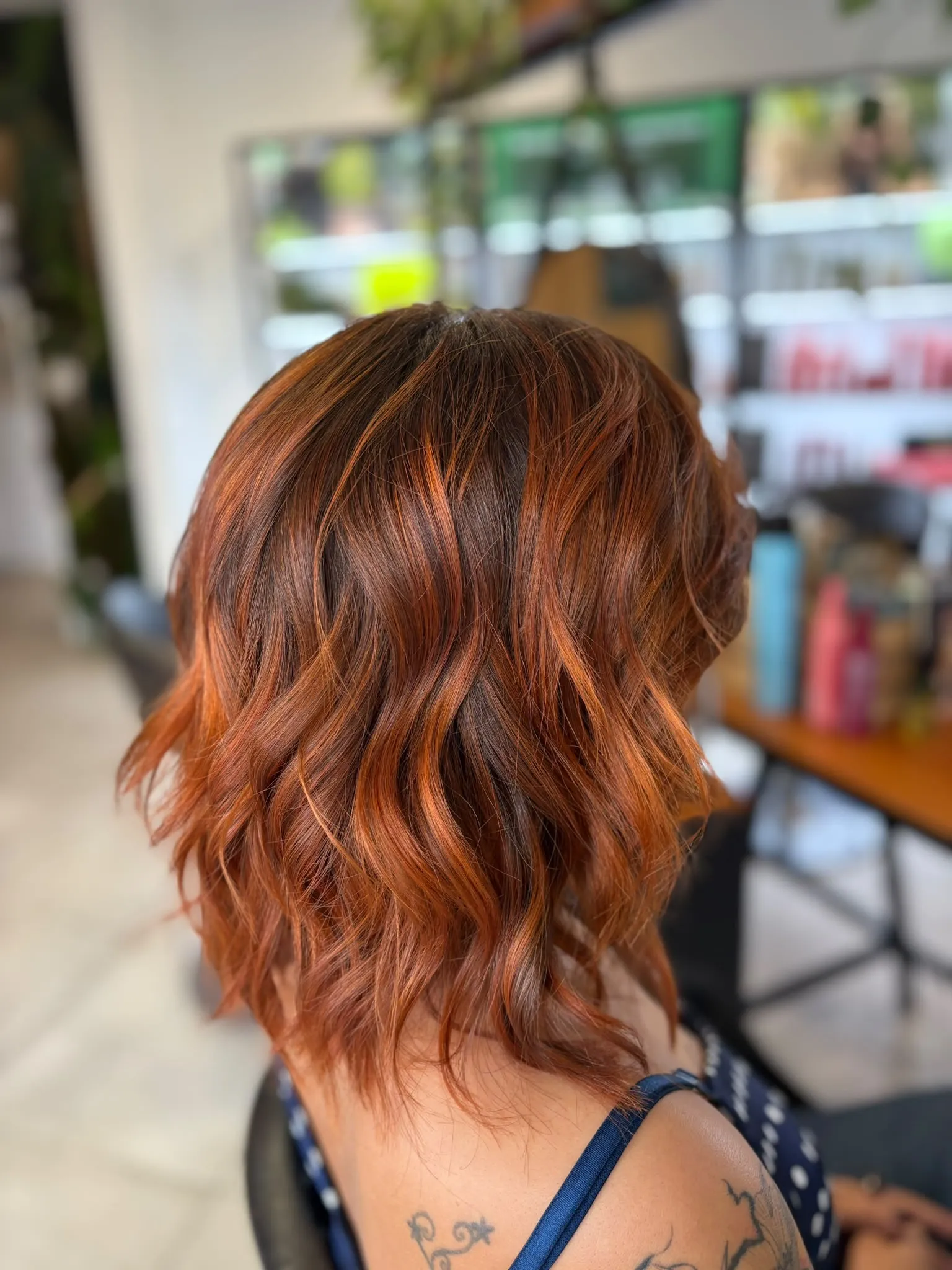 Dos de cheveux mi-longs ondulés d’un roux cuivré aux reflets orangés et racines châtain foncé