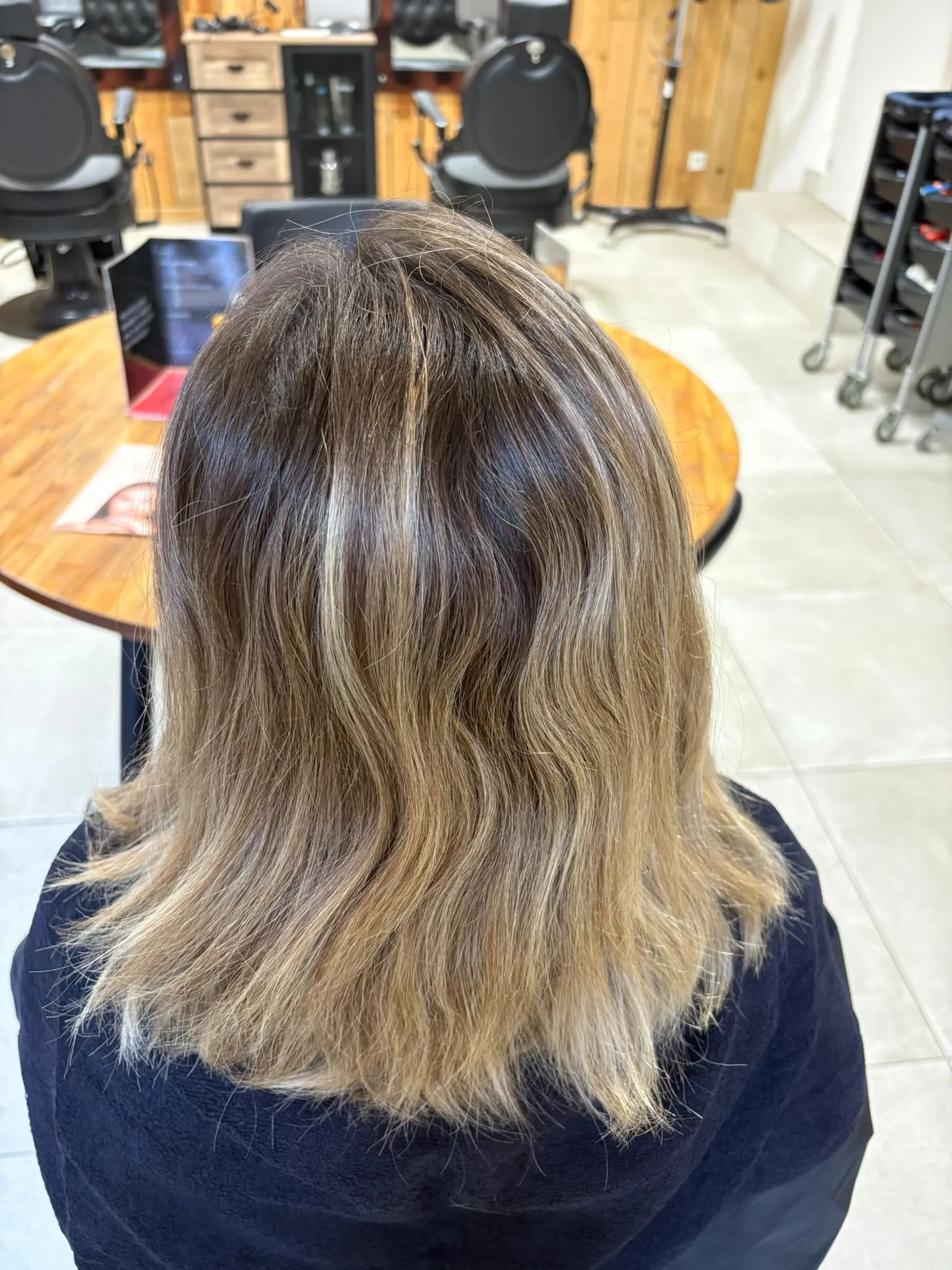 Dos d’une chevelure mi-longue blonde aux racines brunes avant la coloration