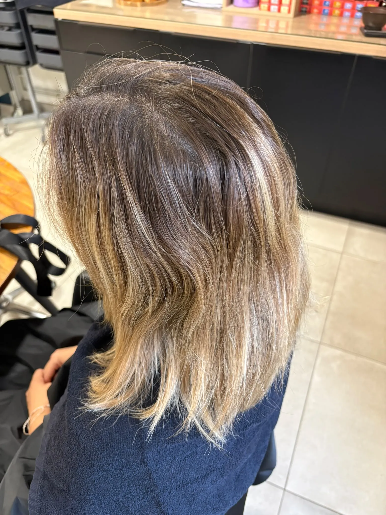 Cheveux mi-longs blonds aux racines brunes, vus de profil avant la coloration
