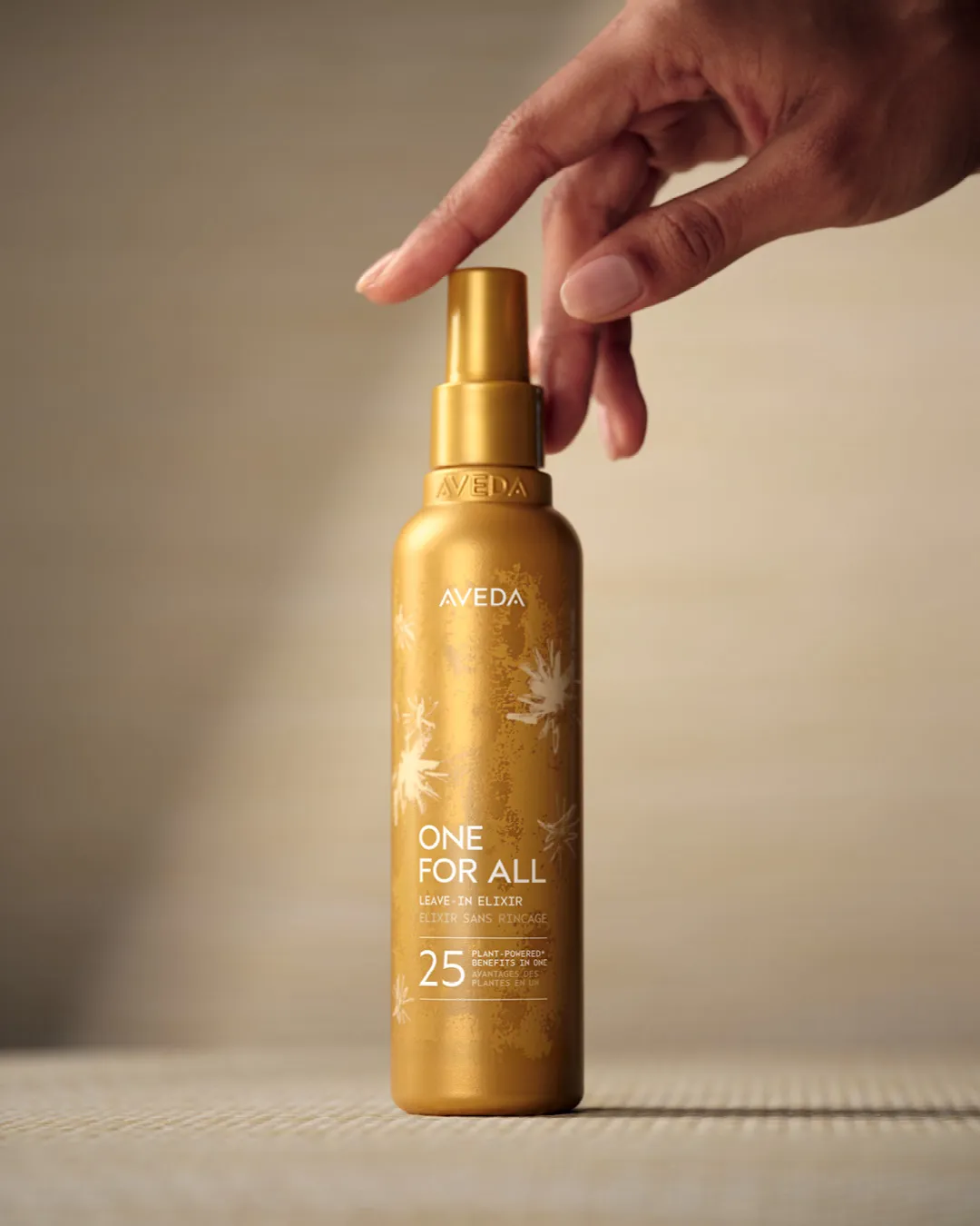 Flacon doré Aveda One for All, un élixir sans rinçage pour les cheveux, tenu par une main