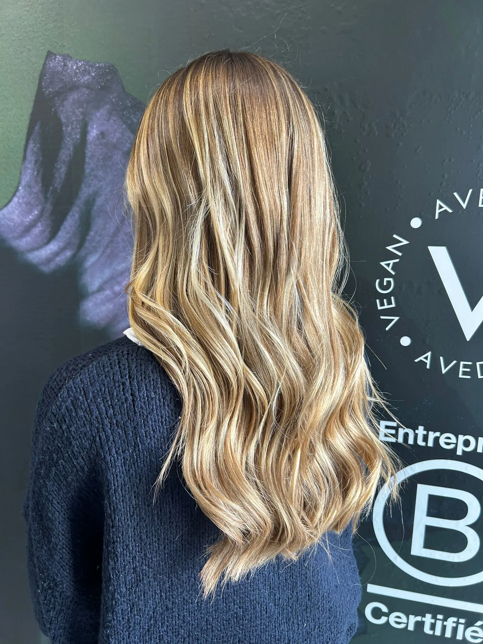 Chevelure blonde ondulée devant une signalétique Aveda
