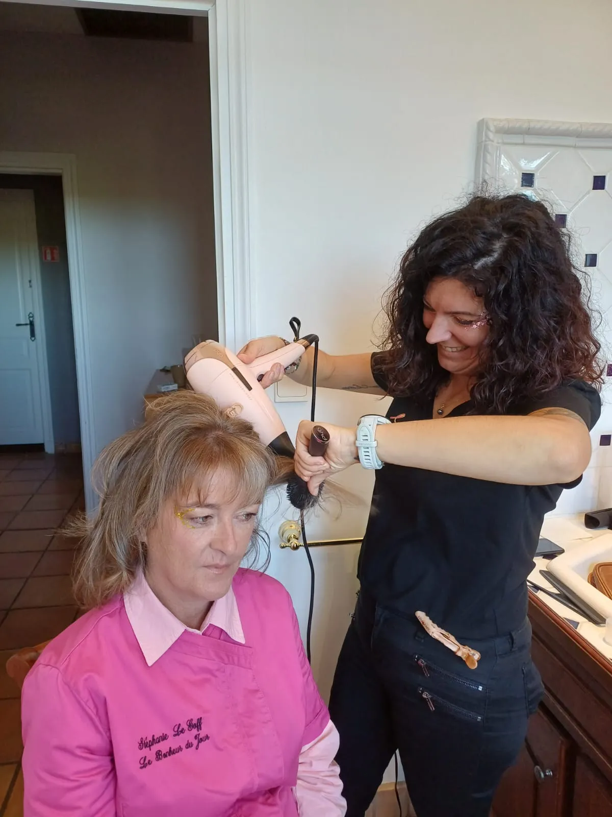 Coiffeuse réalisant un brushing sur les cheveux d’une cliente dans un intérieur chaleureux
