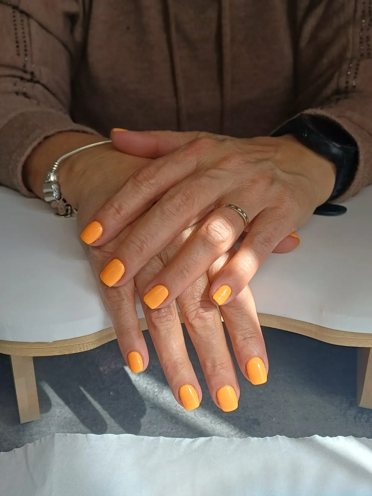 Mains aux ongles courts vernis orange vif posées sur une table