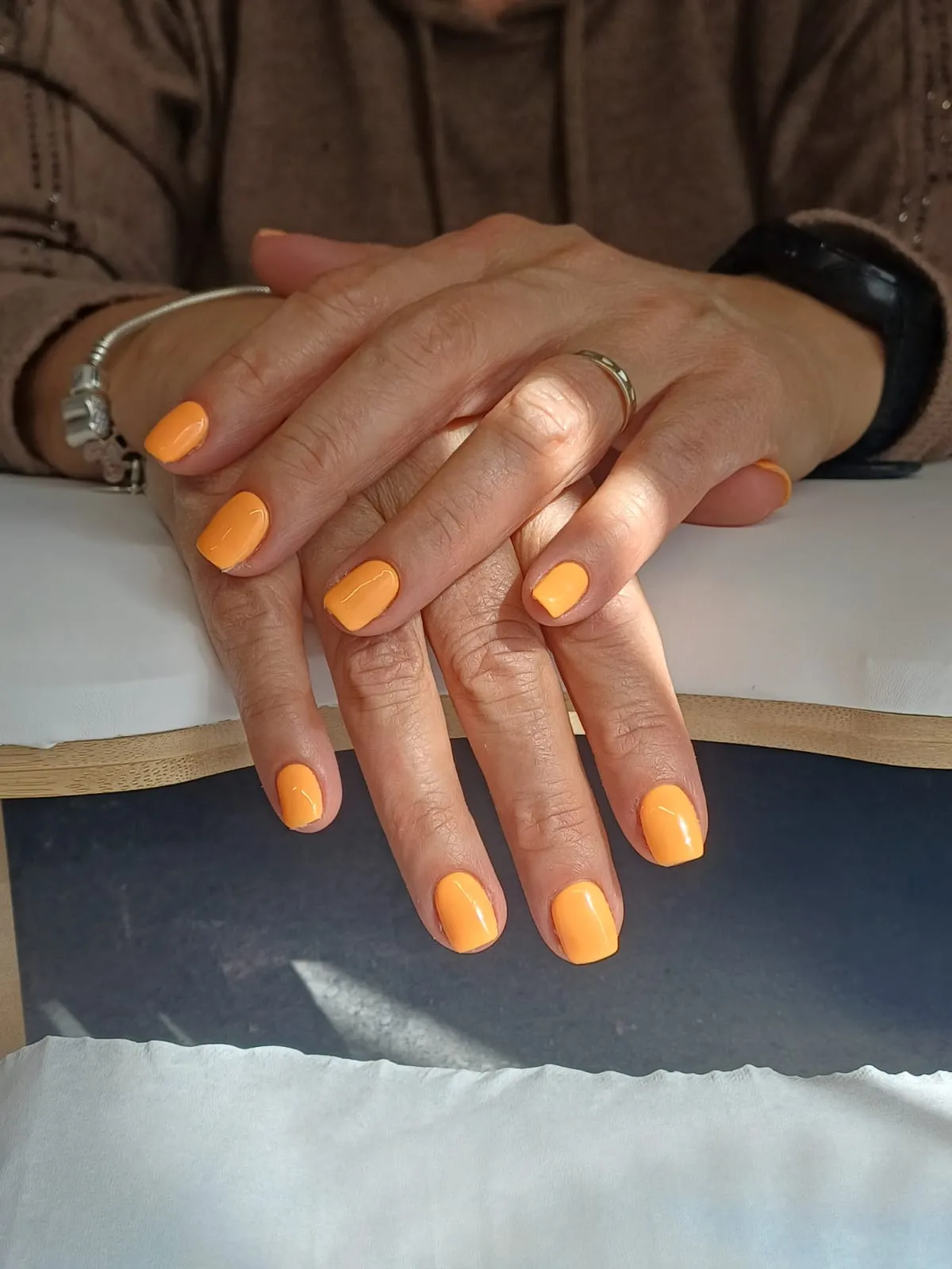 Mains avec des ongles courts recouverts d’un orange brillant
