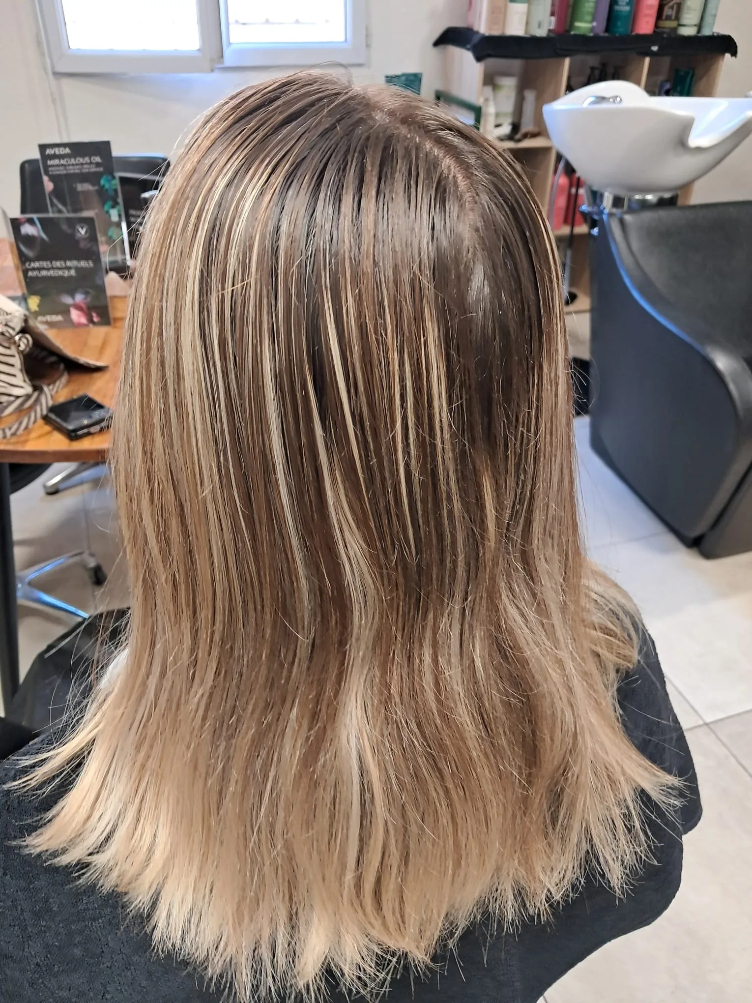 Chevelure mi-longue et lisse avec des mèches blond beige sur une base châtain, vue de dos