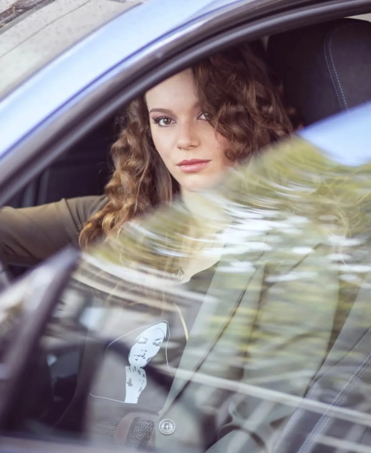 Portrait d’une femme aux cheveux bouclés photographiée à travers la vitre d’une voiture